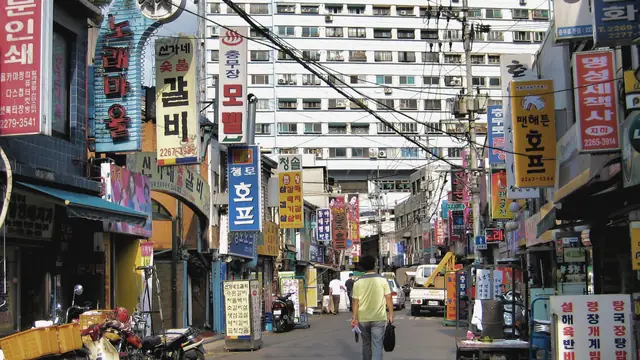 한글 간판이 빽빽한 좁은 길, 카메라 반대쪽으로 걸어가는 남자